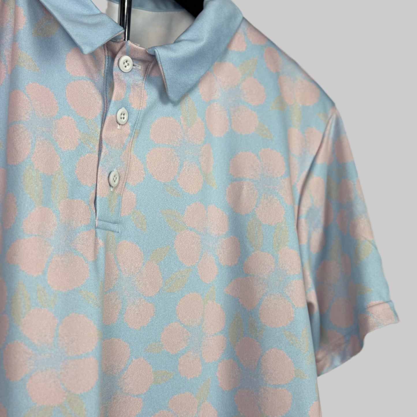 Light blue polo shirt with pink floral pattern on a hanger against a neutral background