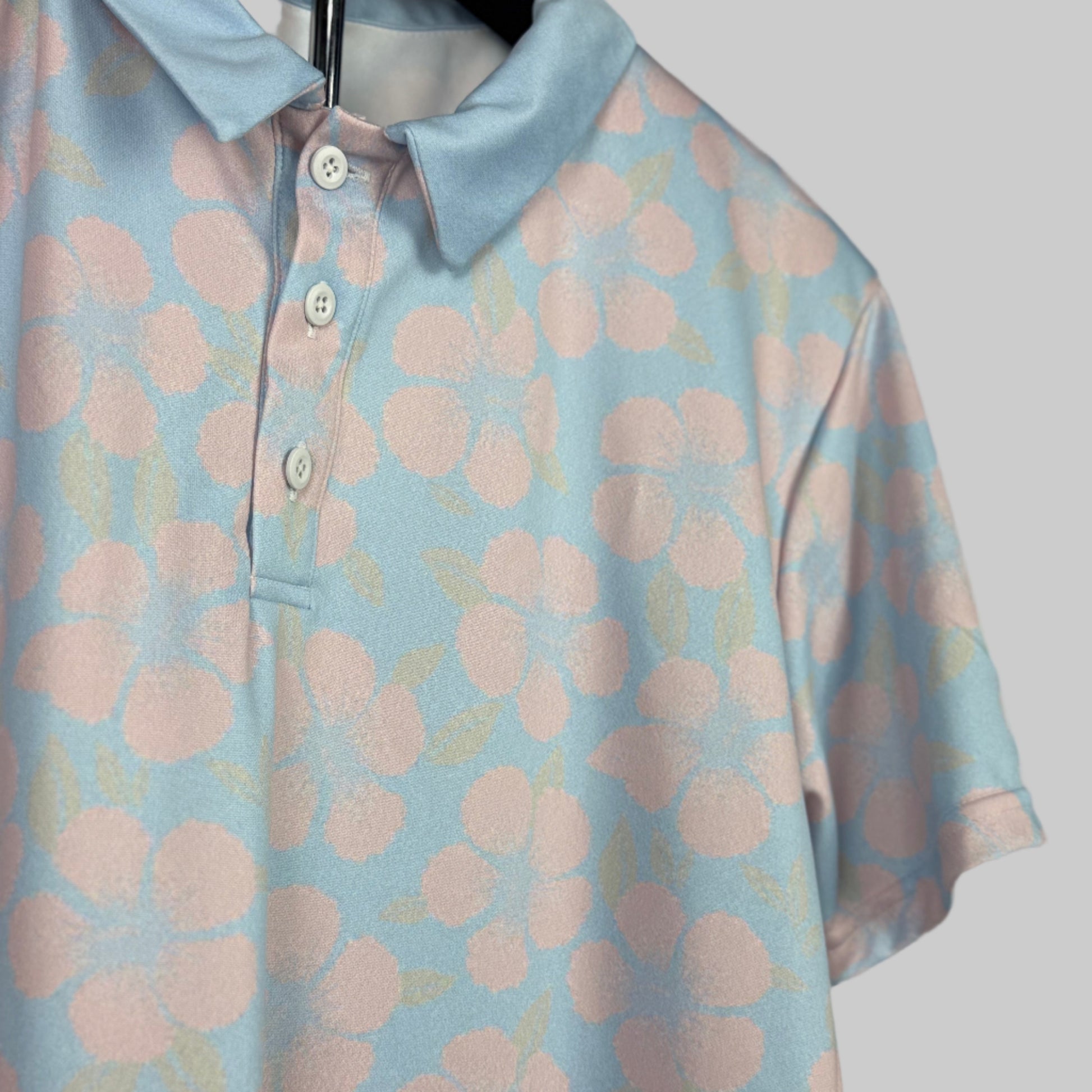 Light blue polo shirt with pink floral pattern on a hanger against a neutral background